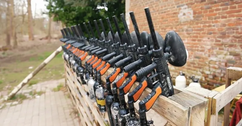 Rangée d'équipements de paintball alignés sur un rack en bois avant l'arrivée d'un groupe