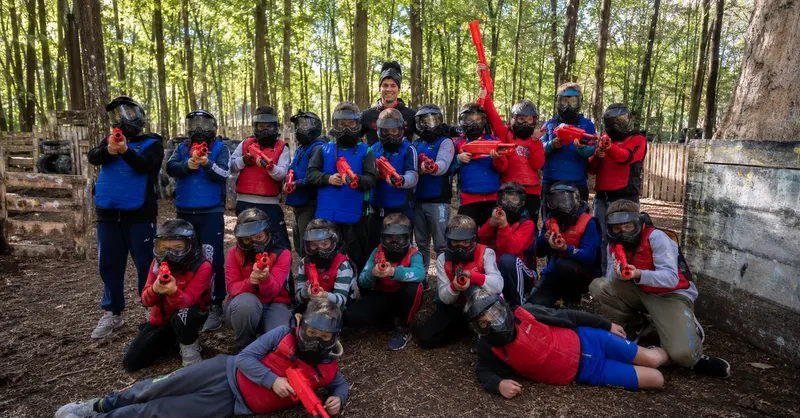 Groupe d'enfants en combinaison et masque posant avec leur équipement après une partie de paintball