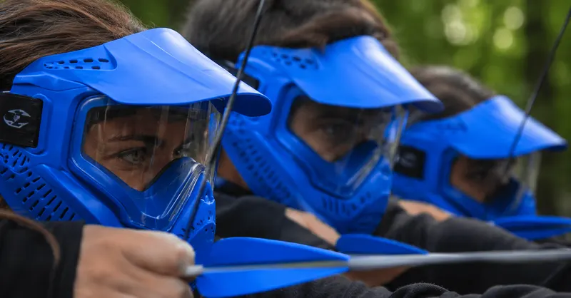 Joueuses en masque intégral bleu, l'une bandant son arc avec une flèche à embout en caoutchouc